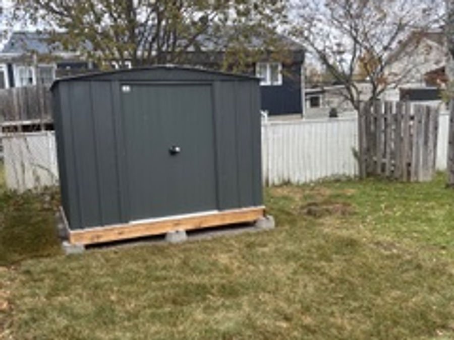 Storage shed installed on a wooden base in a landscaped backyard